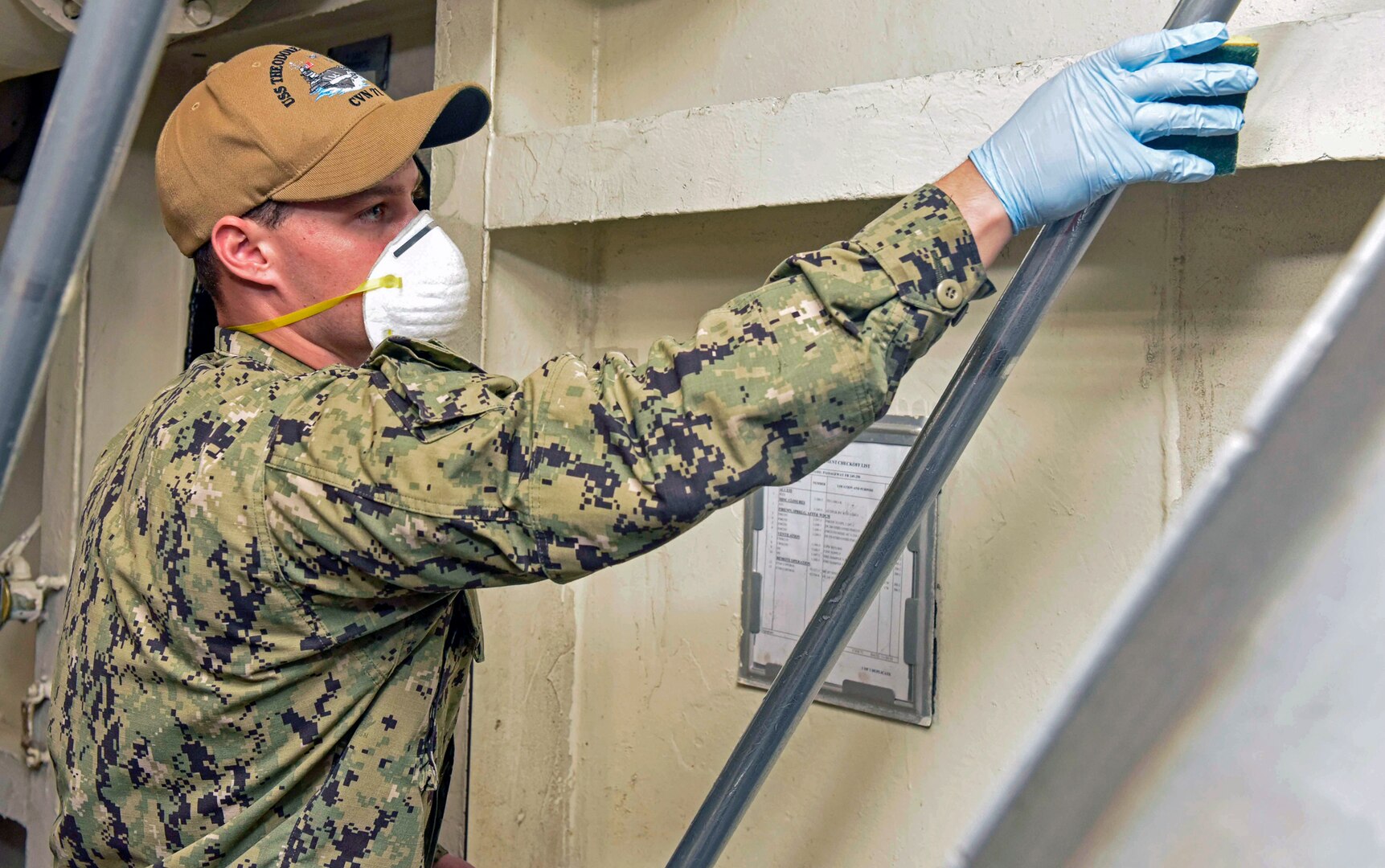 Seaman Airman Preston Rosiere sanitizes a hand rail aboard the aircraft carrier USS Theodore Roosevelt April 19. Upon arriving in Guam March 27, the USS Theodore Roosevelt established an Emergency Command Center, initiated a roving and deep-cleaning team, and continually educated the crew on social distancing and proper protective procedures and behaviors, to assist the crew in mitigating and controlling the spread of COVID.