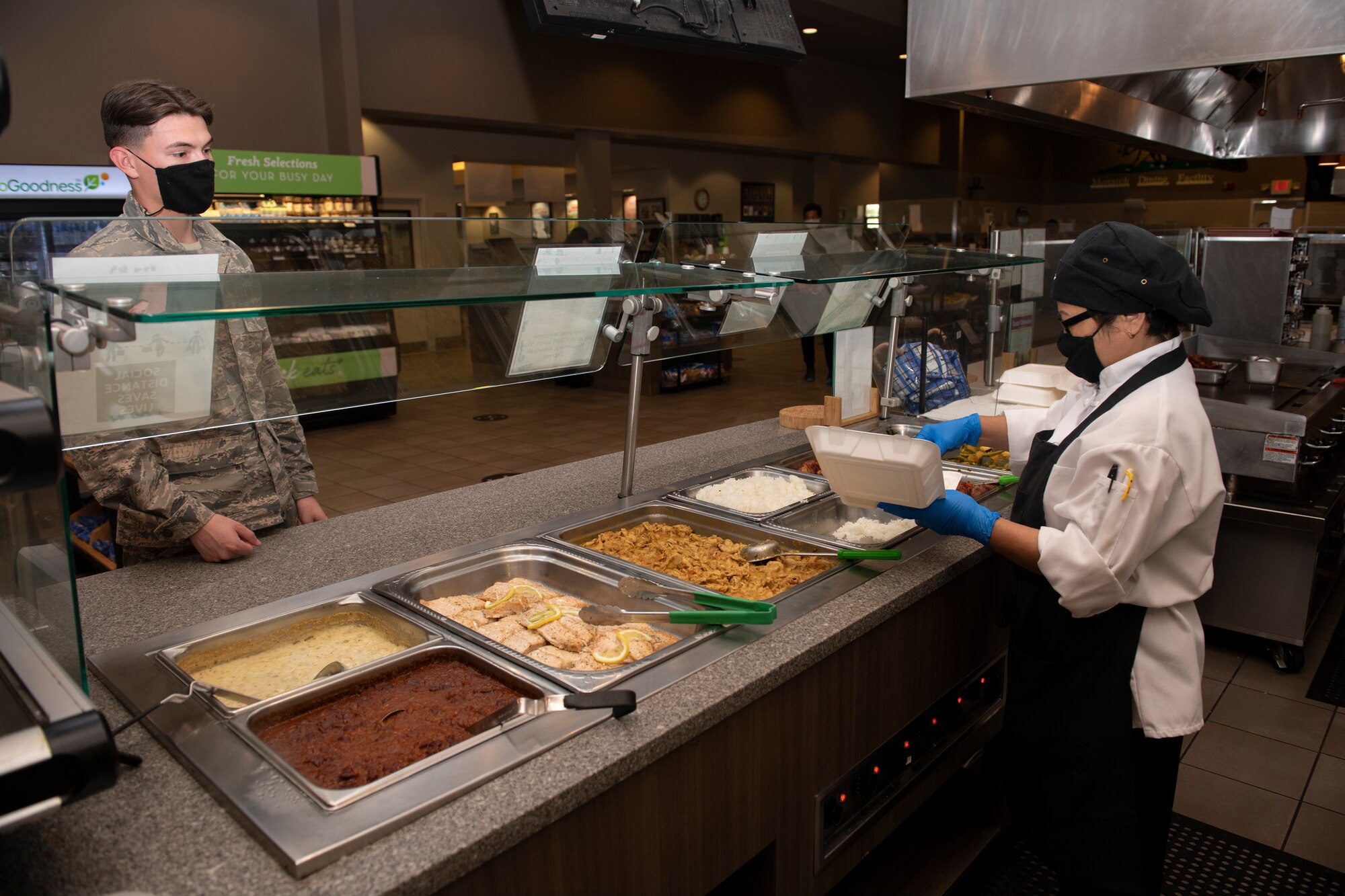 Tessie Santos, Aramark Services cook, serves lunch to an Airman April 24, 2020, inside the Monarch Dining Facility at Travis Air Force Base, California. The Monarch has implemented procedures to prevent the spread of the coronavirus including restricting access to service members only and requiring all patrons to wear masks. (U.S. Air Force photo by Tech. Sgt. James Hodgman)