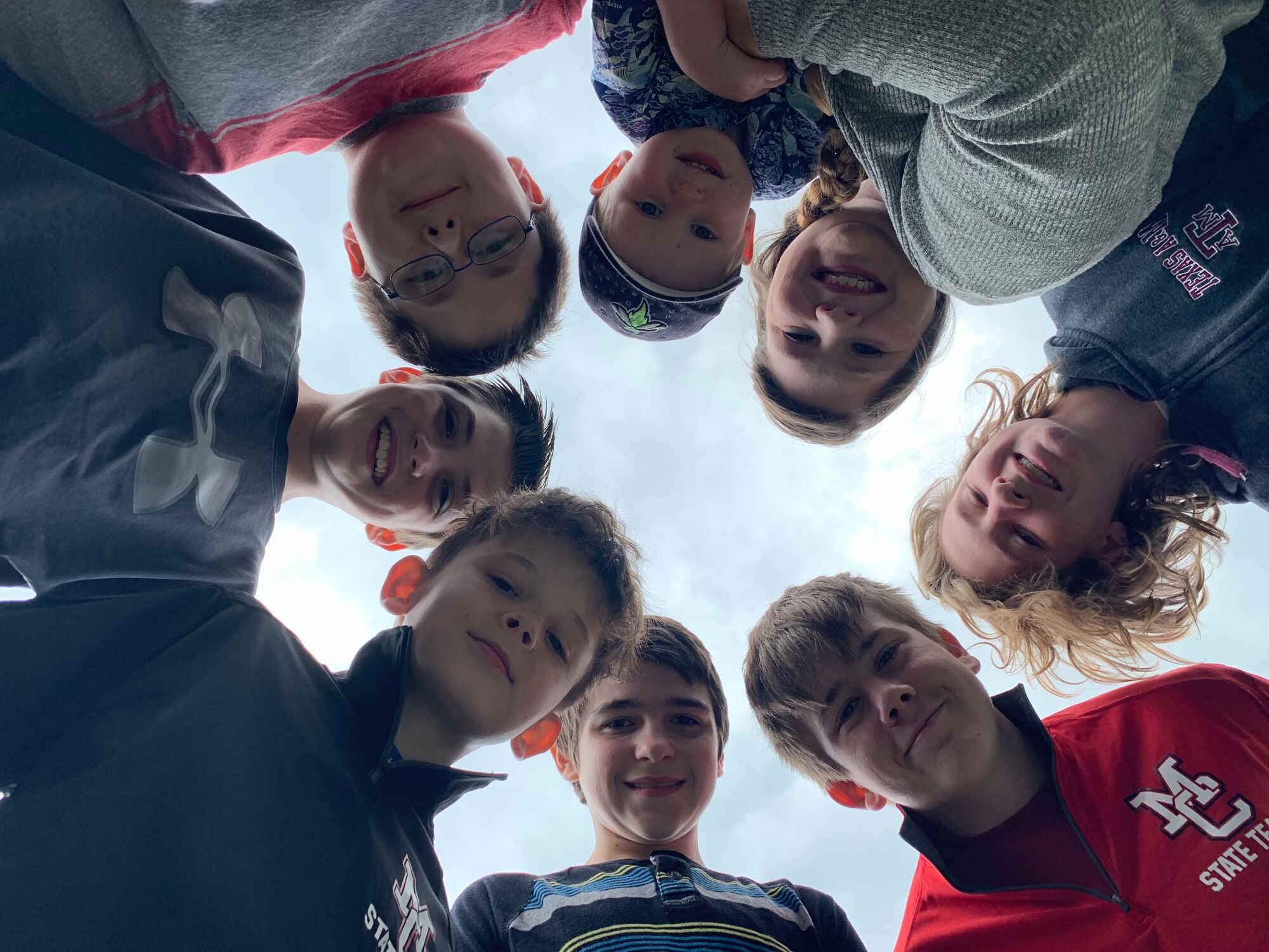 Six boys, aged 11 to 13 gather in a circle as they are photographed from below.