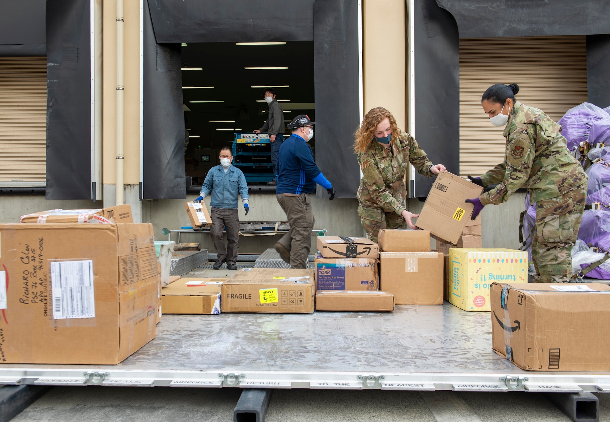 Airman 1st Class Coral Fontanez, Pacific Air Forces Air Postal Squadron mail processing clerk (right), and Airman 1st Class Natalie Shafor (center right), PACAF AIRPS mail processing clerk, load mail onto a pallet at Yokota Air Base, Japan, April 17, 2020. The mail, bound for Misawa Air Base, Japan, was part of a backlog of more than 600 pieces of mail processed through PACAF AIRPS over the past week. (U.S. Air Force photo by Senior Airman Gabrielle Spalding)