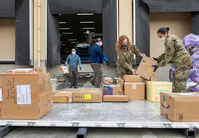 Airman 1st Class Coral Fontanez, Pacific Air Forces Air Postal Squadron mail processing clerk (right), and Airman 1st Class Natalie Shafor (center right), PACAF AIRPS mail processing clerk, load mail onto a pallet at Yokota Air Base, Japan, April 17, 2020. The mail, bound for Misawa Air Base, Japan, was part of a backlog of more than 600 pieces of mail processed through PACAF AIRPS over the past week. (U.S. Air Force photo by Senior Airman Gabrielle Spalding)