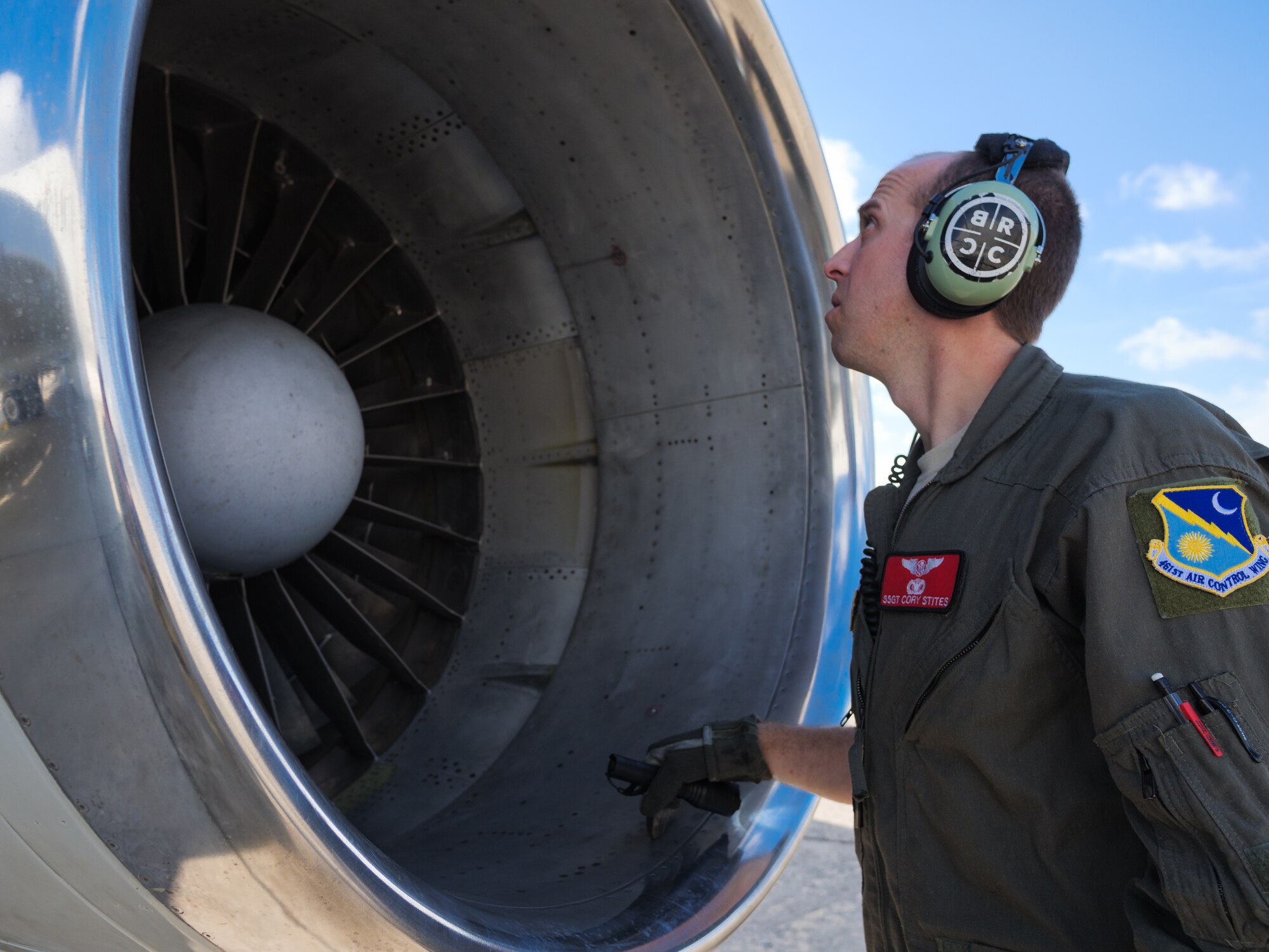 Photo shows a man with ear protection on looking into the parts of an aircraft.