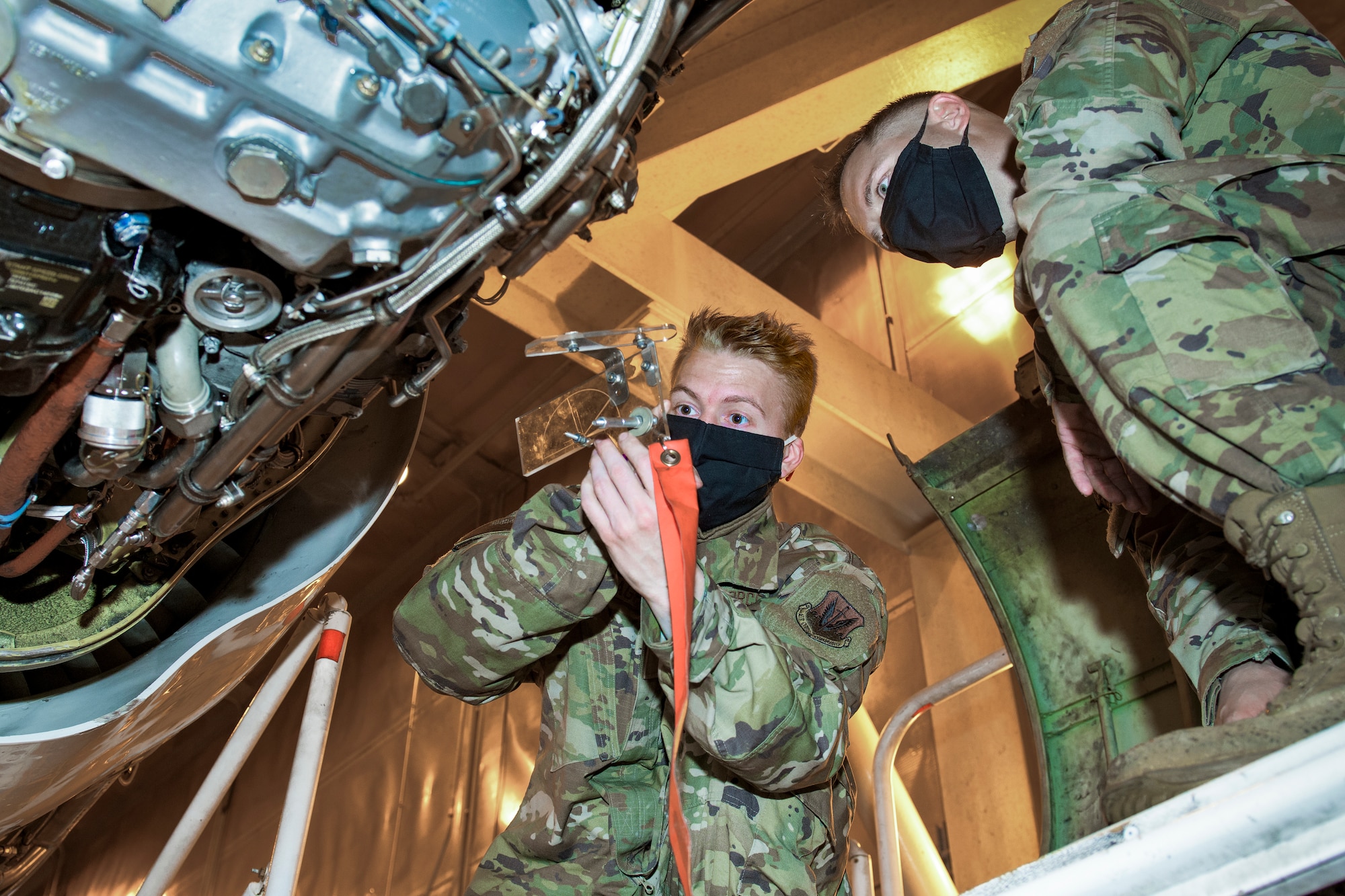 Photo shows two Airmen wearing face masks working on rigging.