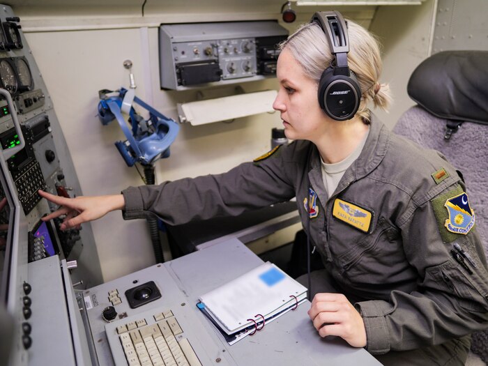 Photo shows a woman on an JSTARS aircraft sitting down and pointing at a screen.