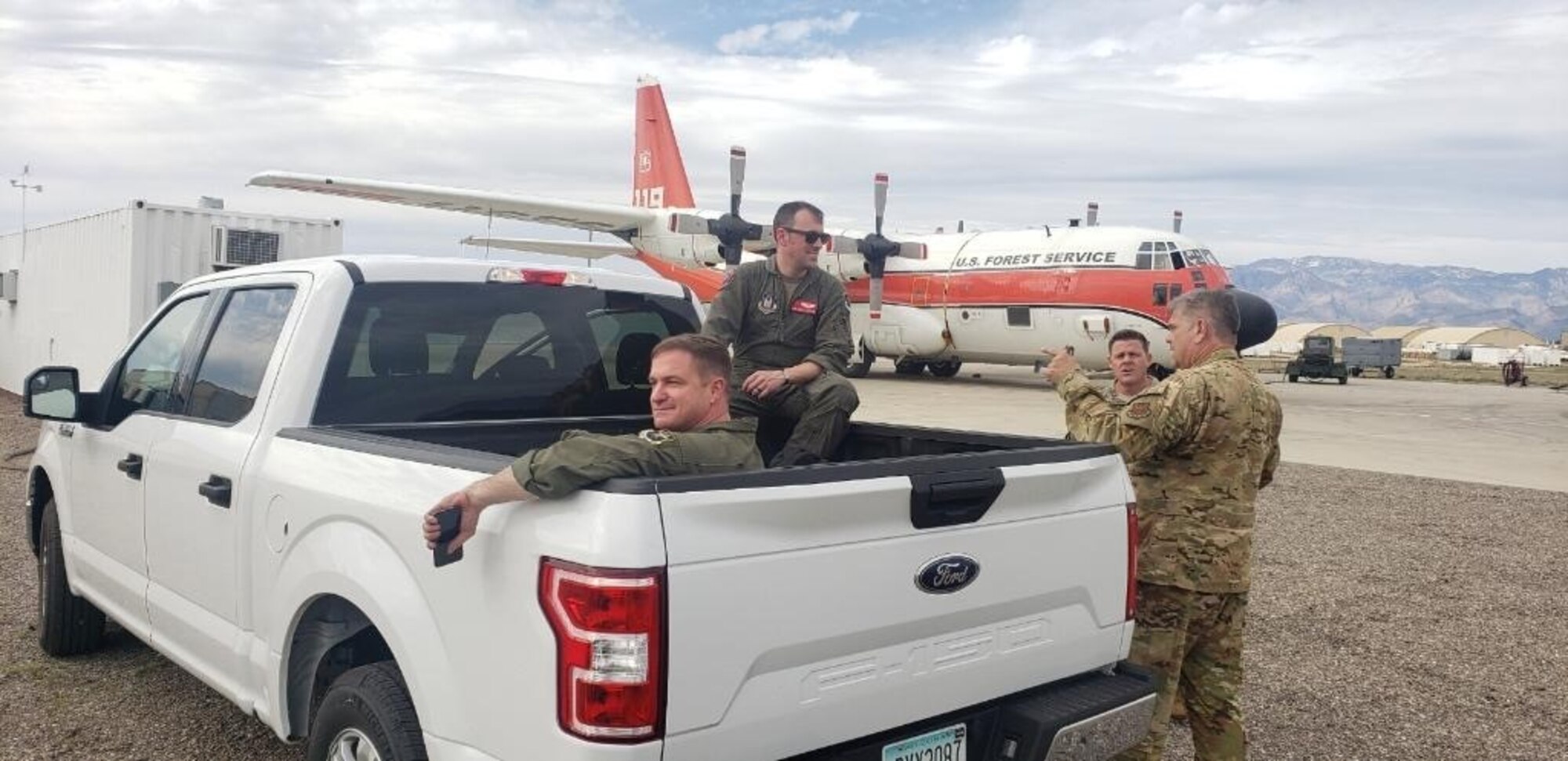 Aircrew sitting in and standing near the bed of a pickup truck.