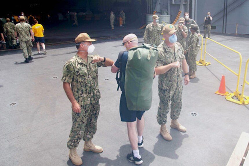 Adm. John C. Aquilino, left, and Fleet Fleet Master Chief, James Honea, right, welcome Hospital Corpsman 1st Class Joshua Graddy, returning from off-ship quarantine, aboard the aircraft carrier USS Theodore Roosevelt (CVN 71), May 2.