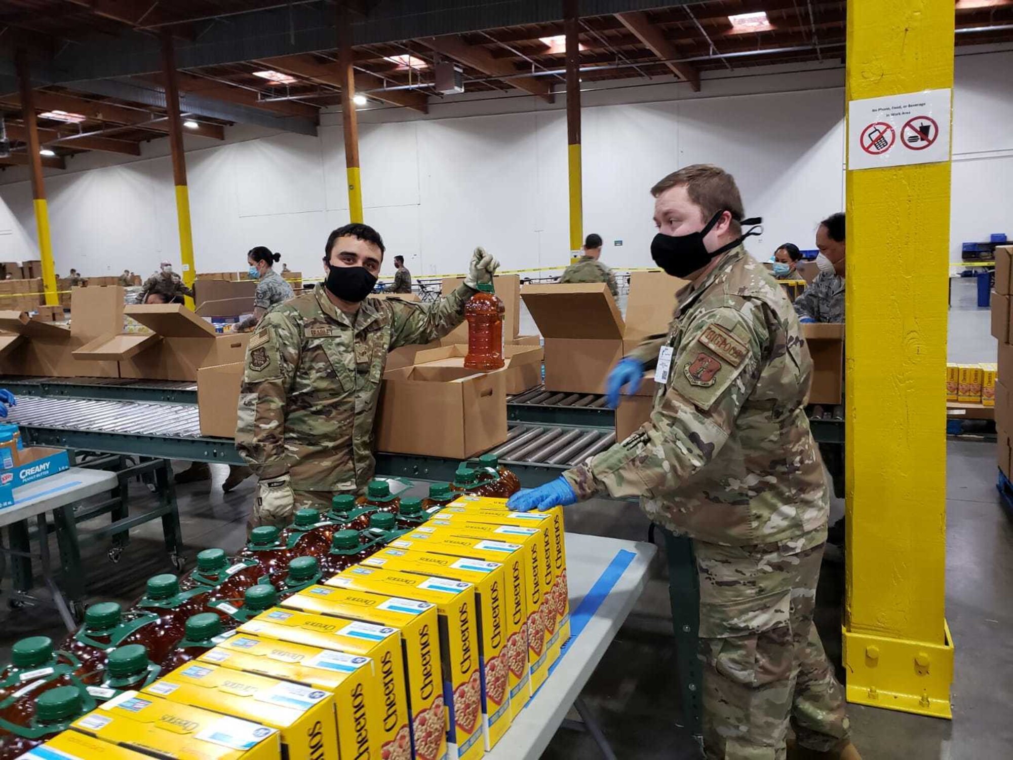 U.S. Air Force Staff Sgt. Matthew Bradley, left, and U.S. Air Force Staff Sgt. Jeremiah Jensen, right, both assigned to the 225th Air Defense Squadron, prepare food boxes at the Food Lifeline COVID Response warehouse April 23, 2020, in Seattle, Washington.  More than 250 Air and National Guardsmen are assigned to the warehouse where they are able to prepare, on average, 268 boxes an hour per line. (U.S. Air National Guard photo)