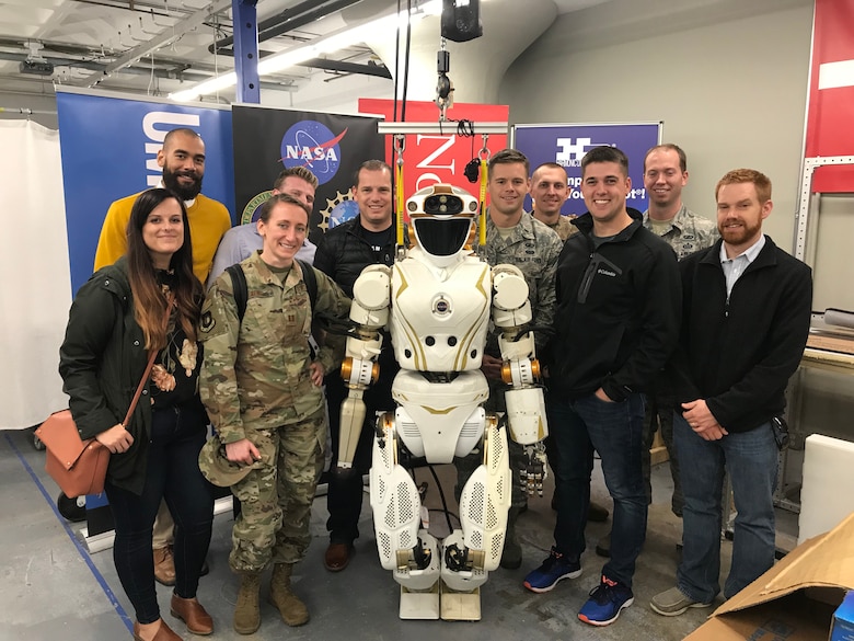 Personnel from the Digital Directorate at Hanscom Air Force Base, Mass., pause for a group photo with the NASA Valkyrie robot during a tour of the MassRobotics facility in Boston, Mass., Oct. 3, 2019.