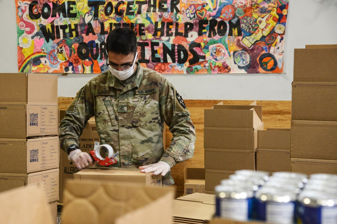 A soldier wearing gloves and a mask tapes a cardboard box closed.