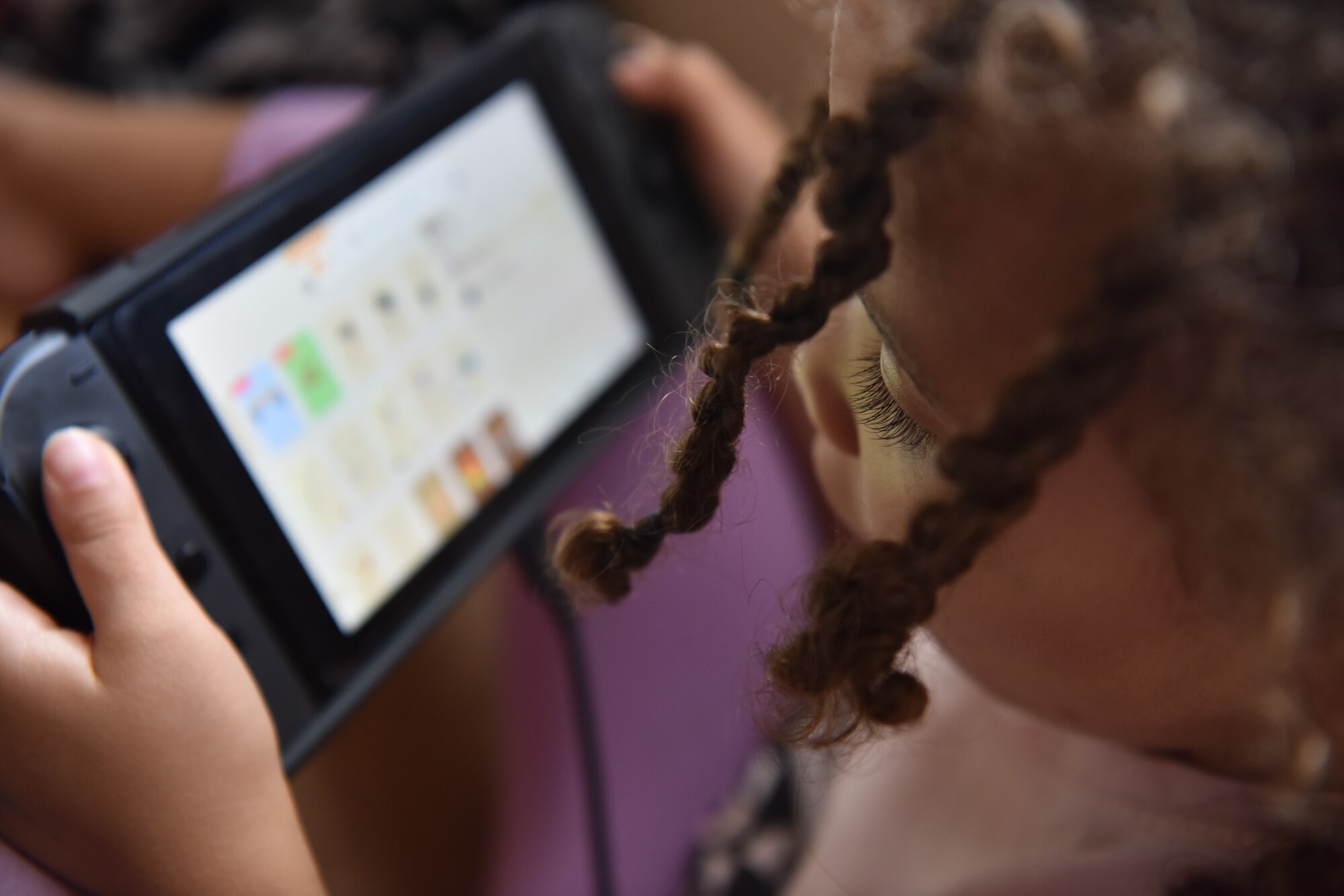 Akira Arzu-Davis, plays a game on a nintendo switch while her father, Airman1st Class Cory J. Davis, a photojournalist  assigned to the 628th Air Base Wing Public Affairs Office, teleworks from home at Joint Base Charleston, S.C., April 29, 2020. Families are encouraged to practice physical distancing during the COVID-19 pandemic. One way to practice physical distancing is by staying indoors.