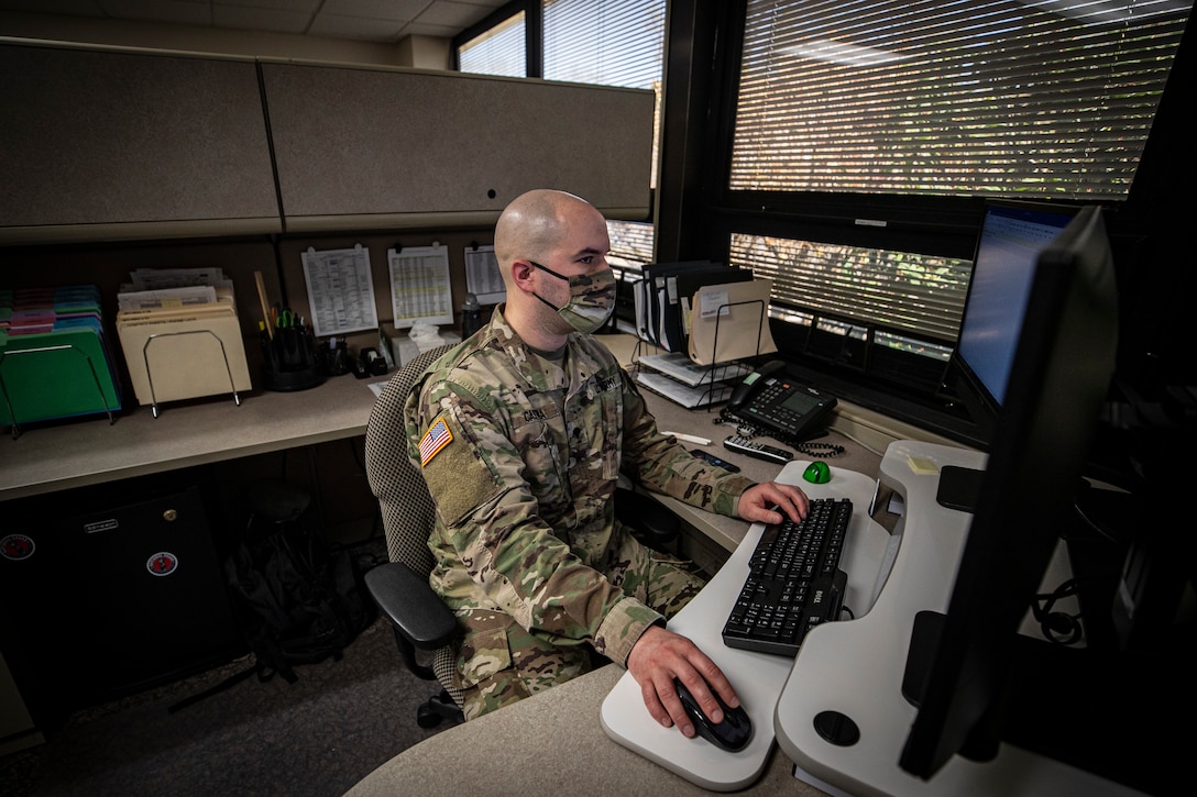 A solider in protective gear works at a computer.