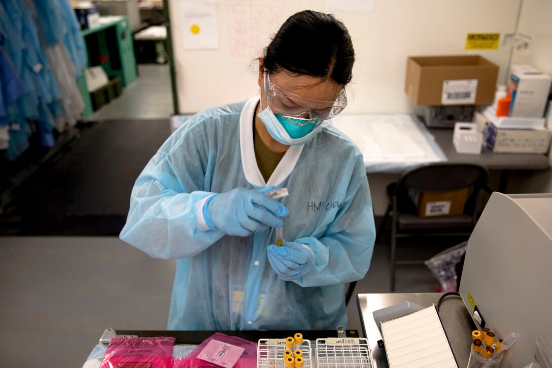 A sailor in medical protective garb handles a vial.