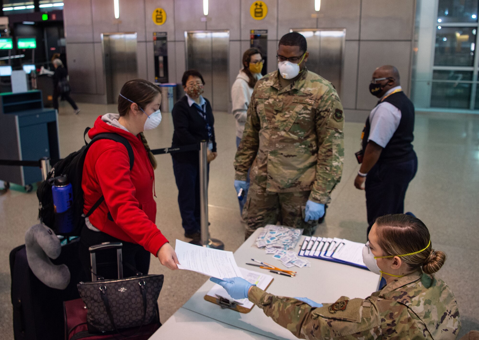 A passenger traveling to Asia, left, hands a medical questionnaire to Airman 1st Class Nicole Mourik, 62nd Aerial Port Squadron passenger service specialist, at the Seattle-Tacoma International Airport in Seattle, Wash., April 30, 2020. In order to travel while still preventing the spread of COVID-19, passengers must answer questions about their current health, where they have traveled recently, and whether they work in a medical facility. (U.S. Air Force photo by Senior Airman Tryphena Mayhugh)