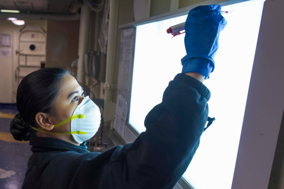 A sailor wearing a mask writes on a screen.