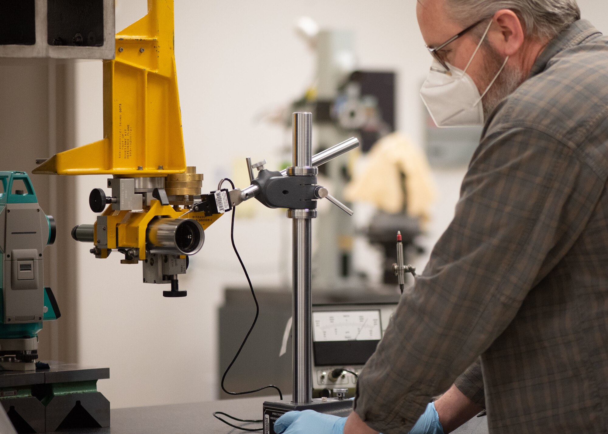 PMEL technician looks at a yellow calibration tool while wearing a face mask