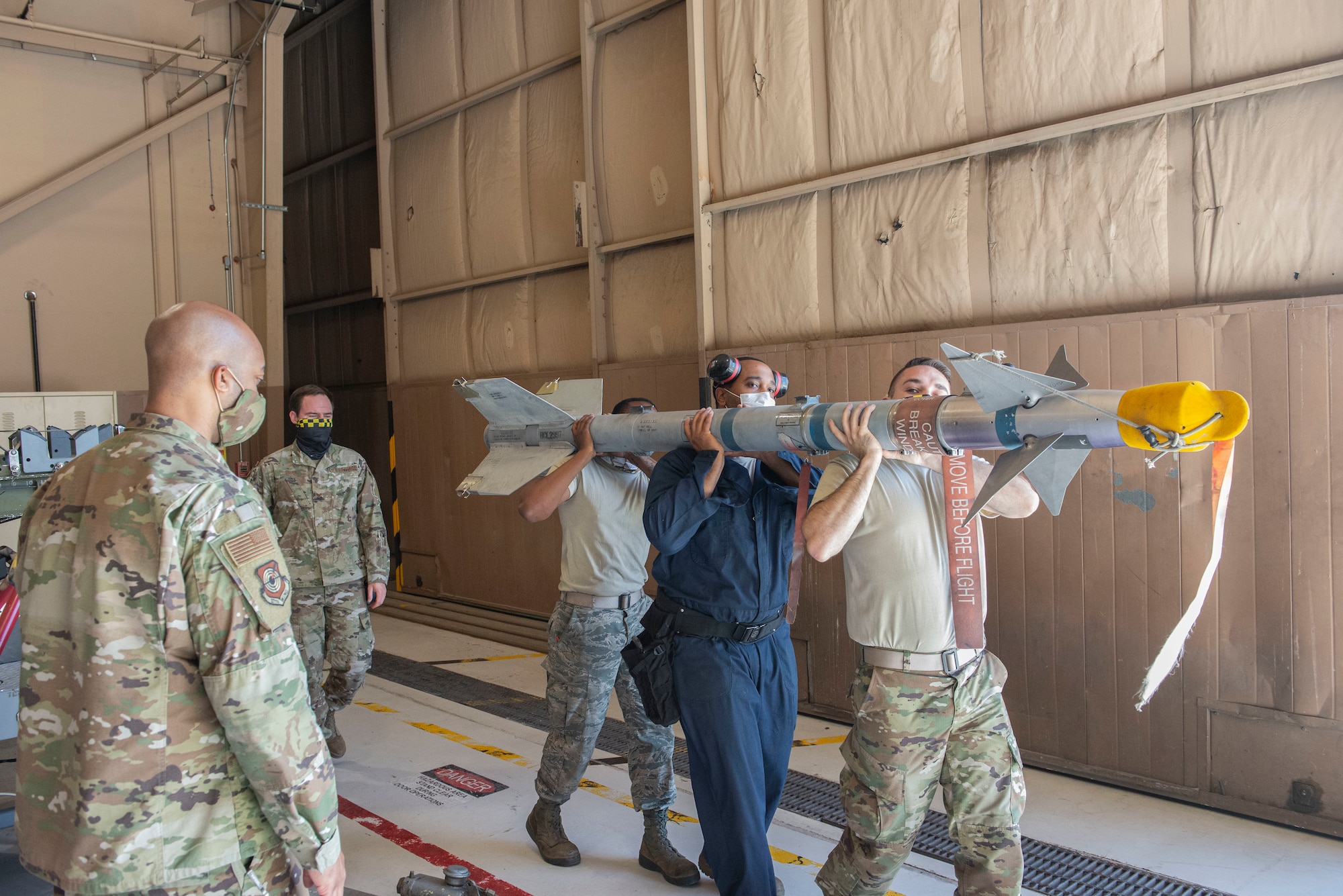 Weapons standardization instructors from the 57th Maintenance Group observe as a weapons load crew moves an AIM-9X training missile onto an F-16 Fighting Falcon.