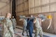 Weapons standardization instructors from the 57th Maintenance Group observe as a weapons load crew moves an AIM-9X training missile onto an F-16 Fighting Falcon.