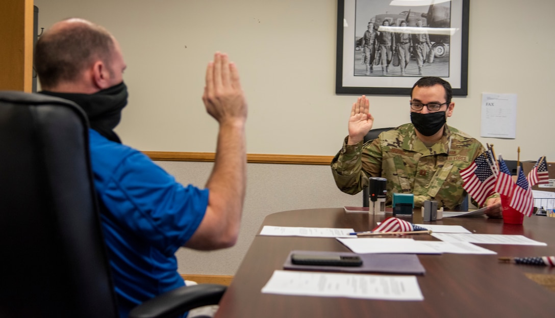 Tech. Sgt. Chuck Broadway, 436th Airlift Wing public affairs NCOIC of media (left), raises his right hand and repeats an oath from Capt. Marc Nevenis, 436th Airlift Wing Legal Office chief of military justice (right), May 1, 2020, at Dover Air Force Base, Delaware. Personnel wear cloth masks and practice social distancing while conducting appointments to reduce the spread of COVID-19. (U.S. Air Force photo by Airman 1st Class Jonathan Harding)