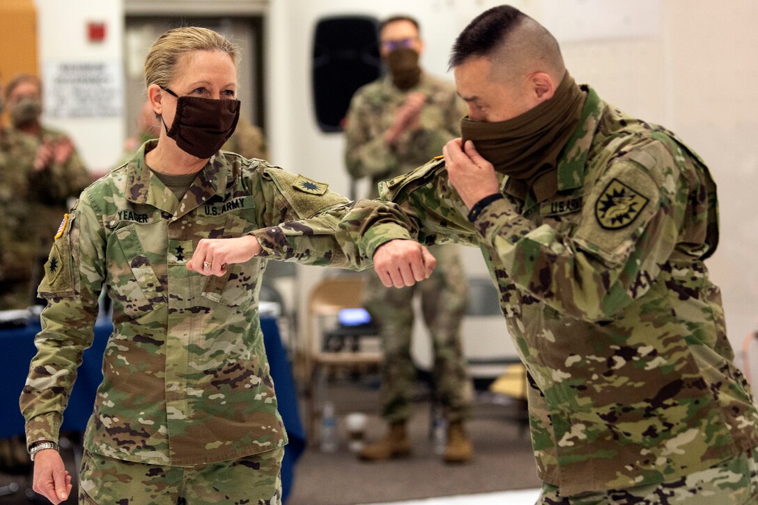 Two soldiers wearing face masks elbow bump each other.