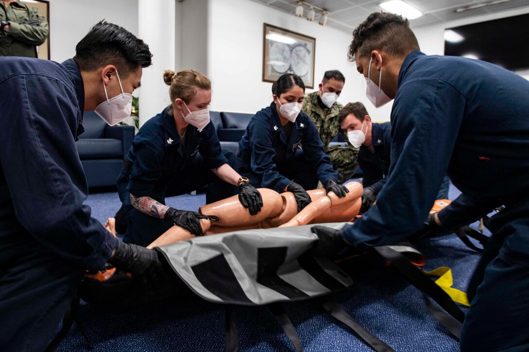 Service members use a mannequin to train how to put someone onto a stretcher.