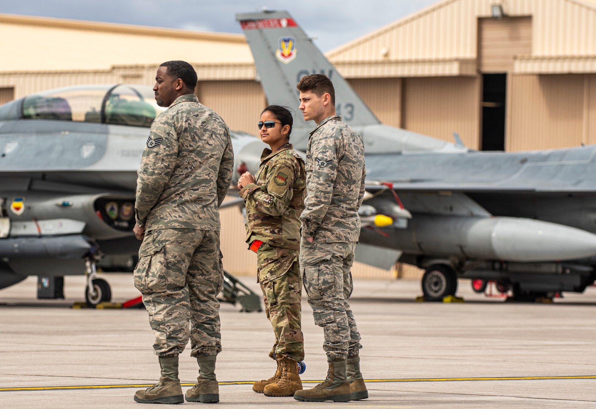 A group of Airmen stand on the flightline looking off in the distance.