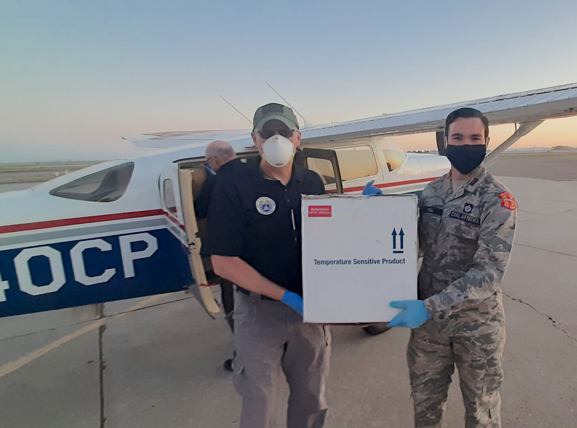 New Mexico Civil Air Patrol Maj. Gregory Griffith, left, and Flight Officer Casey Neal carry a package of COVID-19 test kits from the CAP aircraft to a vehicle for transport from Albuquerque International Airport to a laboratory for processing.