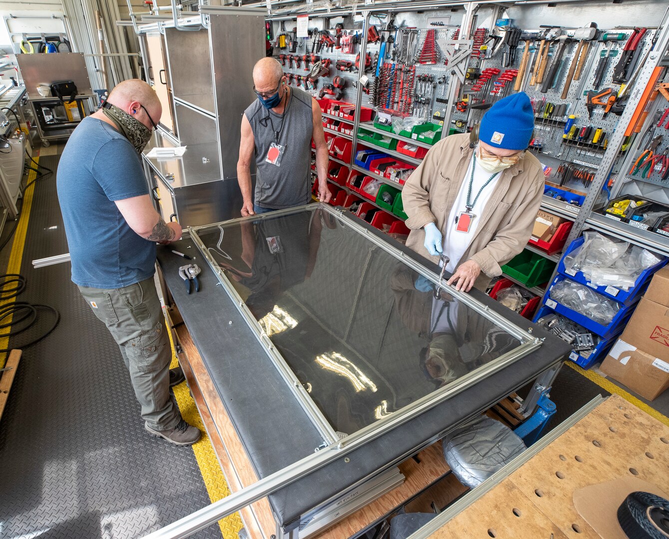 Jared David (left), Tracy Atkins (center) and Harlen Caldwell (right) assemble clean barrier made from vinyl in the Moonshine Lab at Puget Sound Naval Shipyard & Intermediate Maintenance Facility May 4. This team is part of a cadre of innovators taking on the challenge of designing and building protective barriers for customer facing interactions within the shipyard.