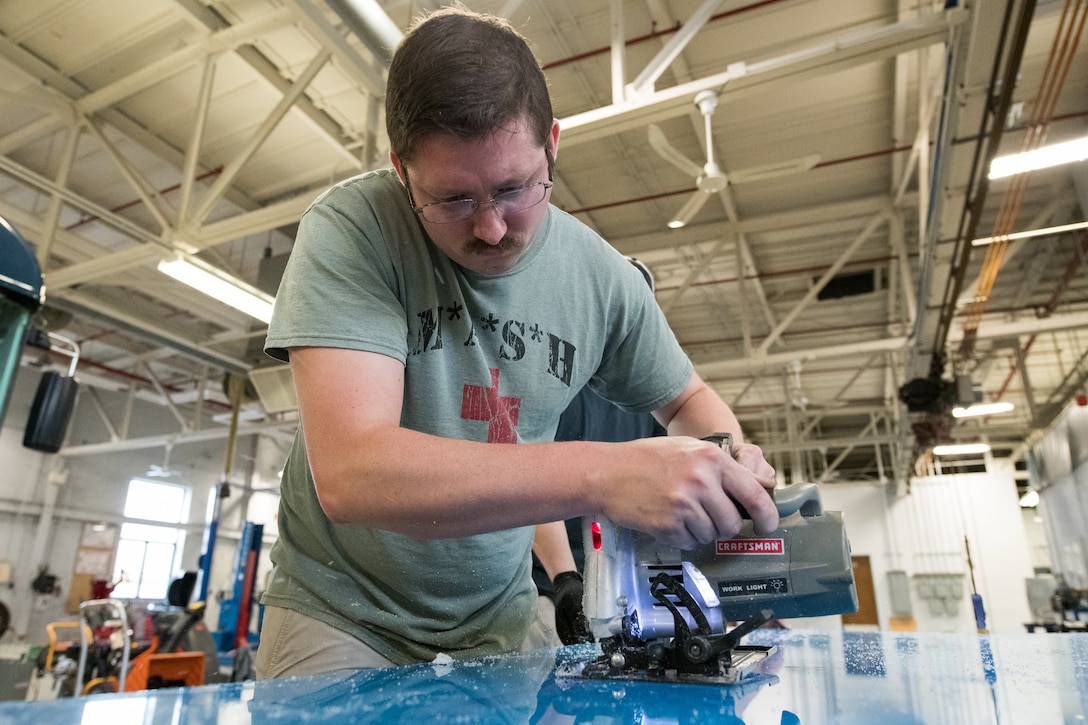 Staff Sgt. Cory Nelson, 436th Logistics Readiness Squadron Ground Transportation Support noncommissioned officer in charge, cuts a sheet of plexiglass to be fitted into a transport bus April 27, 2020, at Dover Air Force Base, Delaware. Despite being off duty, Nelson meticulously measured and cut each piece to ensure a proper fit. The installation of plexiglass barriers on transport buses further mitigates the spread of COVID-19, protecting the health and safety of 436th LRS Airmen and aircrew.  (U.S. Air Force photo by Mauricio Campino)