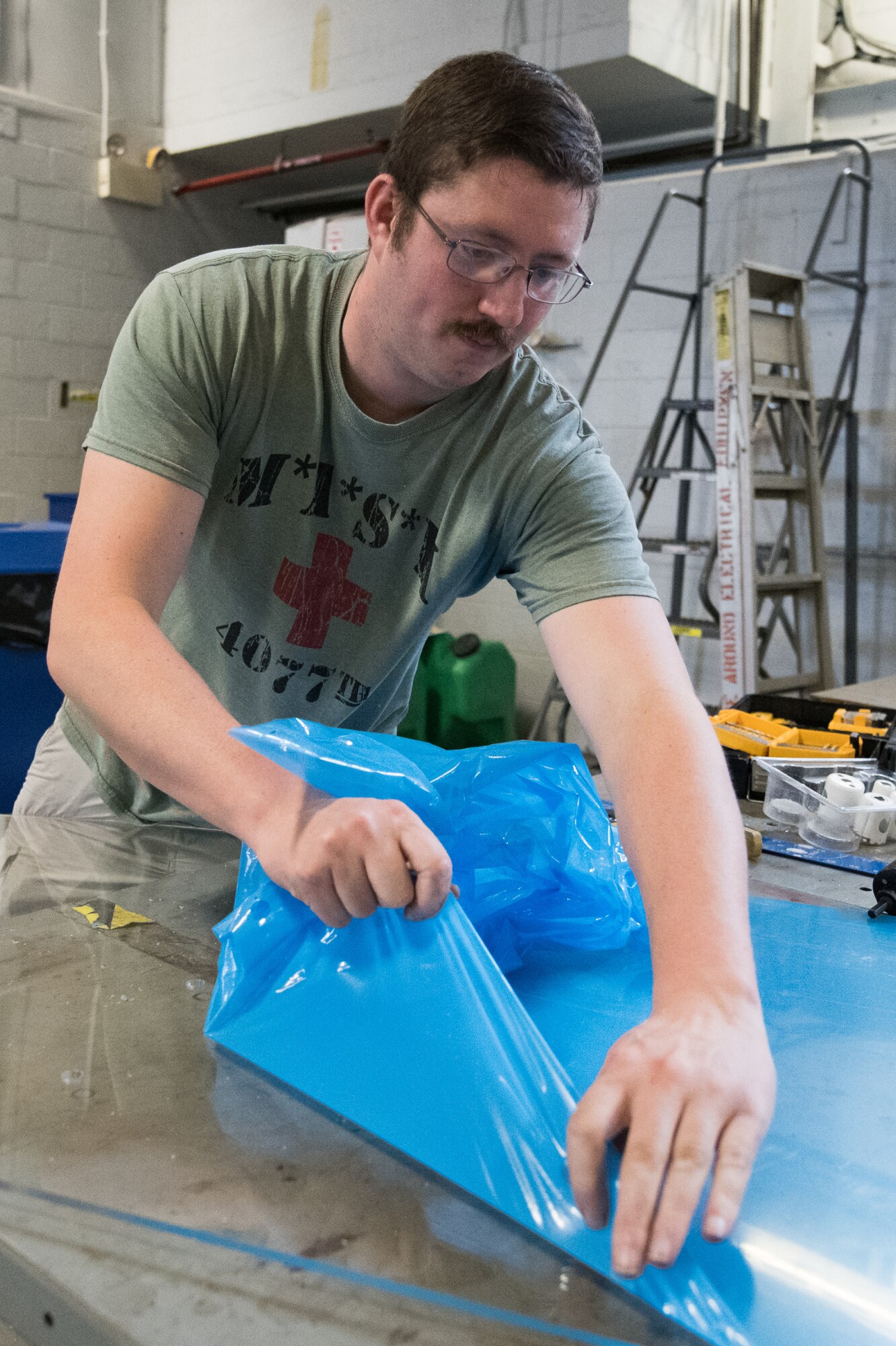 Staff Sgt. Cory Nelson, 436th Logistics Readiness Squadron Ground Transportation Support noncommissioned officer in charge, removes the protective cover from a sheet of plexiglass April 27, 2020, at Dover Air Force Base, Delaware. Despite being off duty, Nelson meticulously measured and cut each piece to ensure a proper fit. The installation of plexiglass barriers on transport buses further mitigates the spread of COVID-19, protecting the health and safety of 436th LRS Airmen and aircrew. (U.S. Air Force photo by Mauricio Campino)