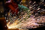 Sparks fly off of metalwork. A worker wears a protective hood.