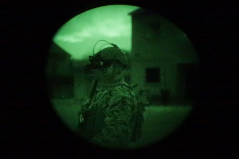 Through a camera lens, a Marine can be seen wearing night vision goggles.