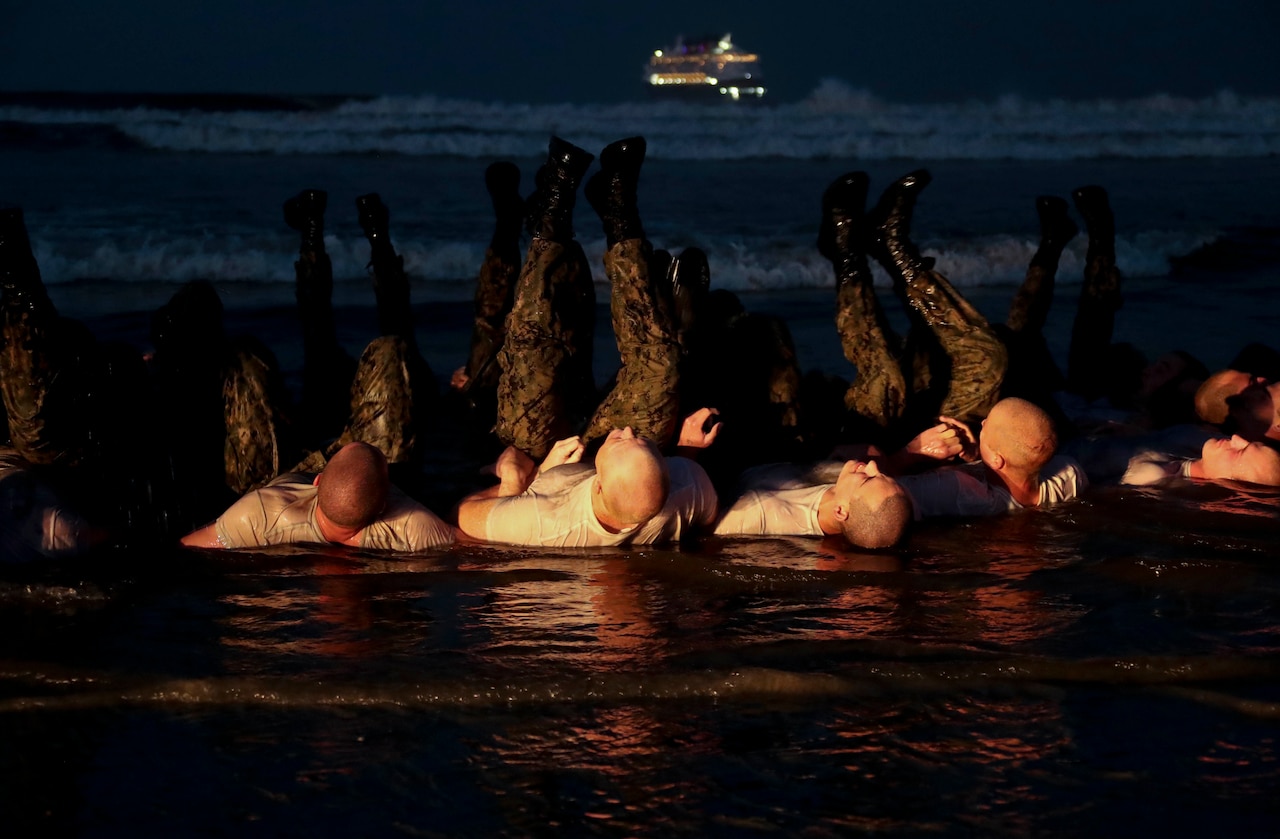 SEAL candidates exercise on the sand as the surf washes over them.