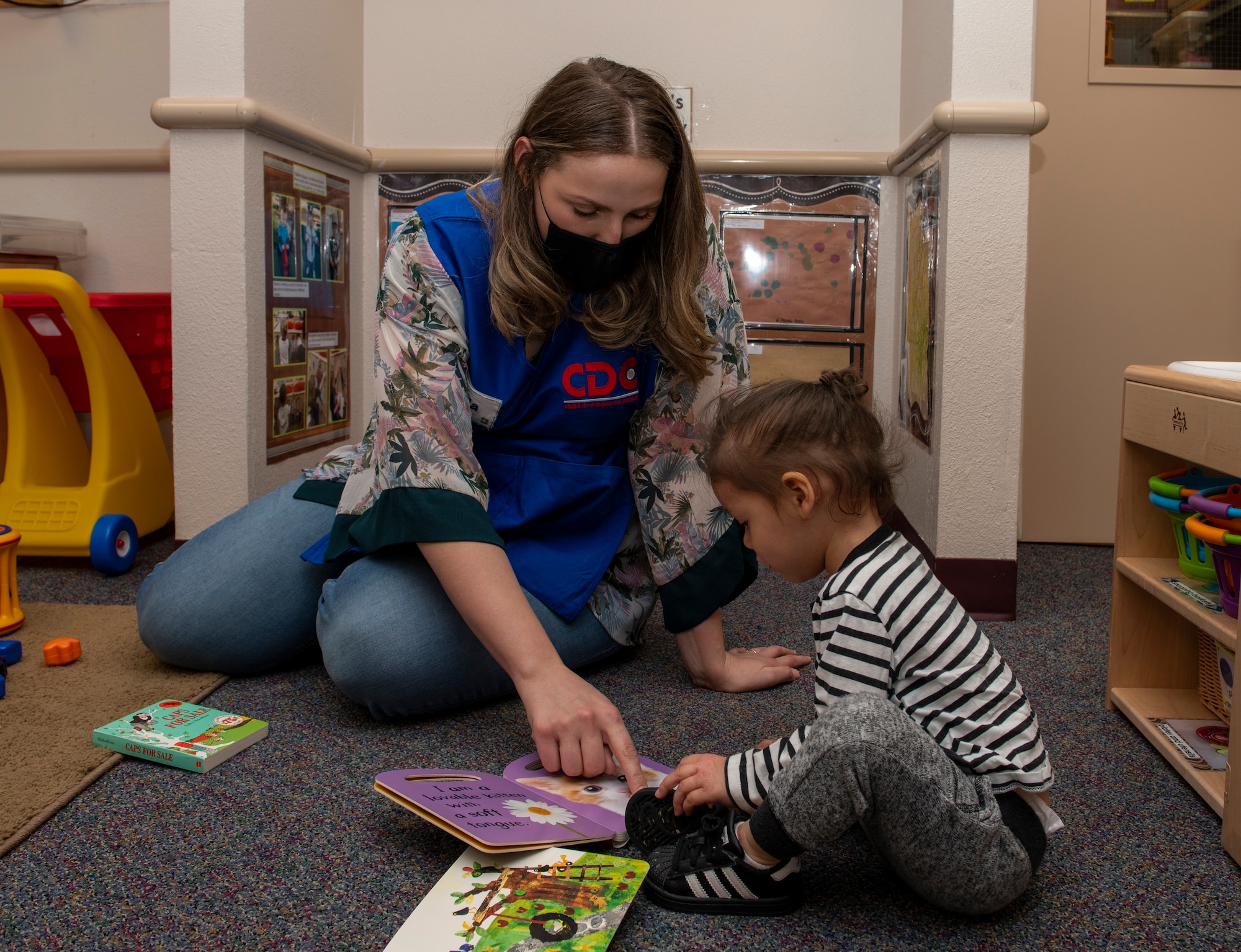 Emilia Williams, 60th Force Support Squadron child and youth program technician, helps a child read a book May 1, 2020, inside Child Development Center 3 at Travis Air Force Base, California. Travis AFB has three childcare centers that have cared for children during the coronavirus pandemic. (U.S. Air Force photo by Tech. Sgt. James Hodgman)