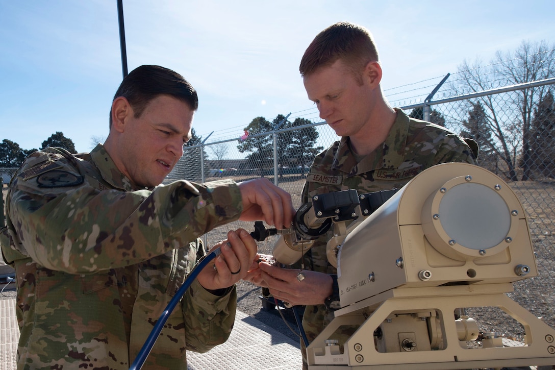 Two airmen work on an antenna.