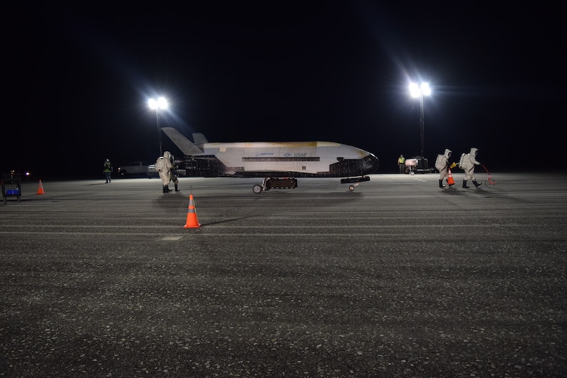 Three people dressed in head-to-toe protective gear walk away from a small military plane sitting on a runway.