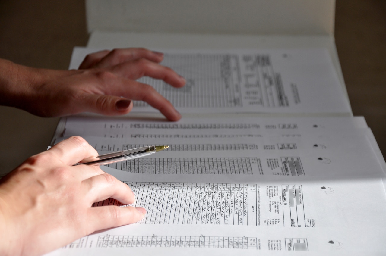 Two hands rest on paperwork; one hand holds a pen.