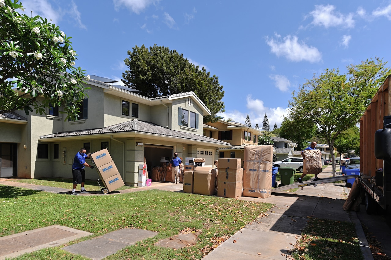 Workers move boxes out of a home. Many other boxes sit on a driveway.