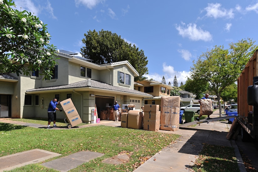 Workers move boxes out of a home. Many other boxes sit on a driveway.