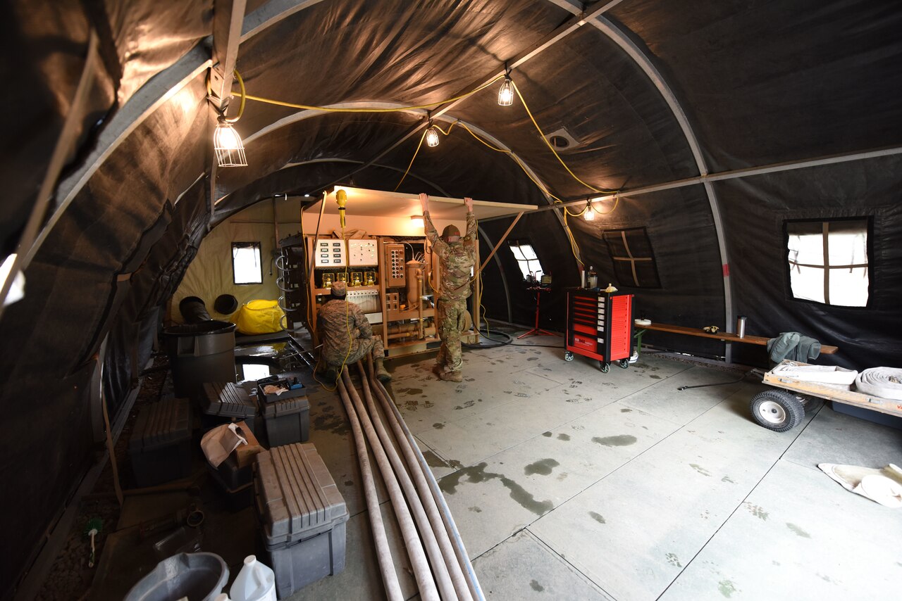 Two airmen train on  a water purification system inside a tent.