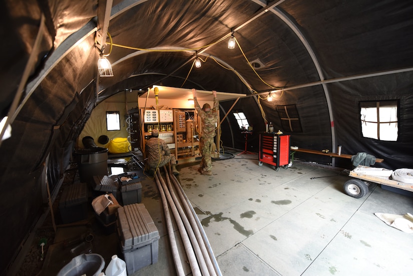 Two airmen train on  a water purification system inside a tent.