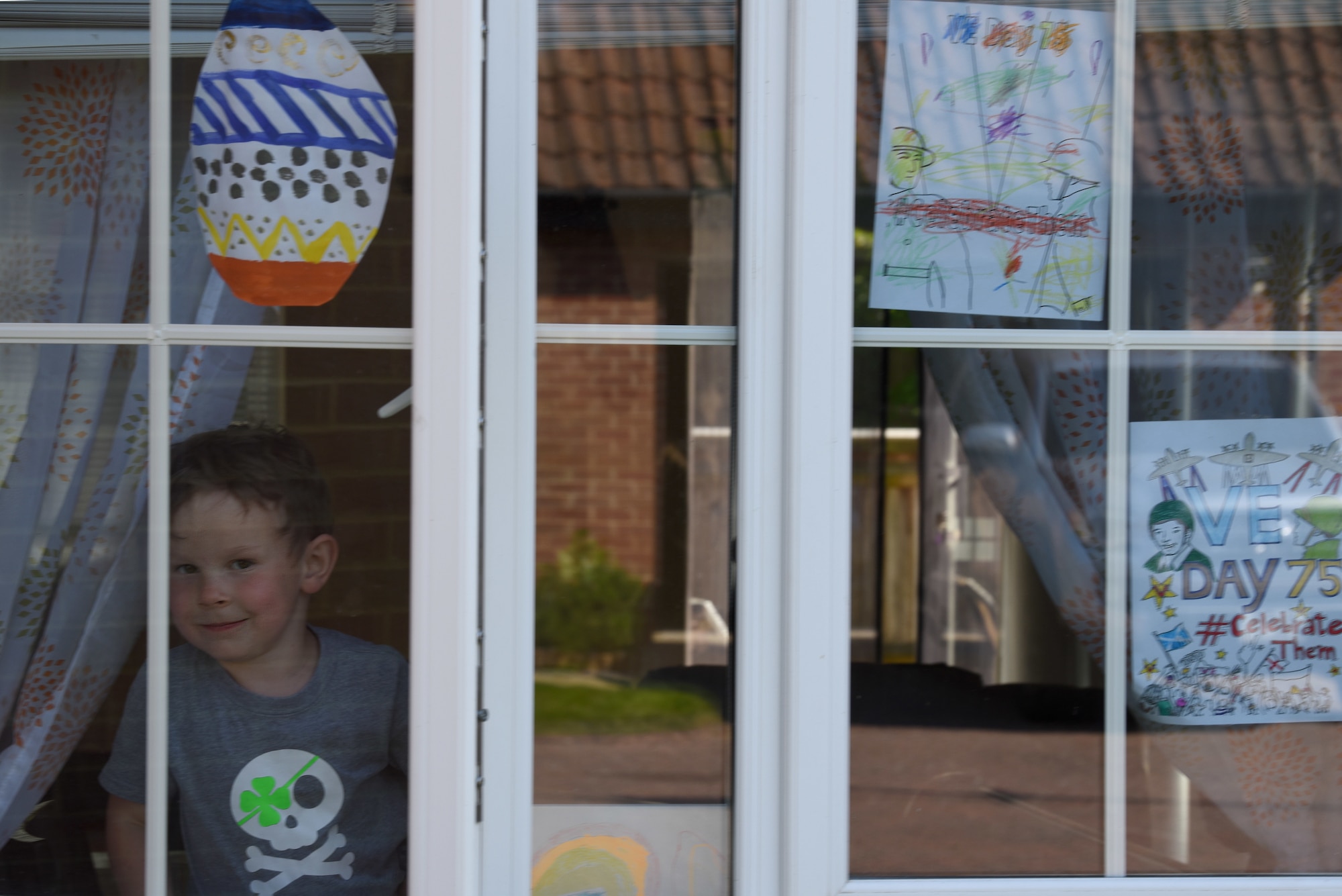 A child of a U.S. Air Force Airman displays Victory in Europe Day artwork in their window in Liberty Village at Royal Air Force Lakenheath, England, May 6, 2020. VE Day marked the end of World War II and serves as a day of reflection and to commemorate the bravery of the men and women who ushered in freedom across Europe. (U.S. Air Force photo by Airman 1st Smith Rhonda Smith)