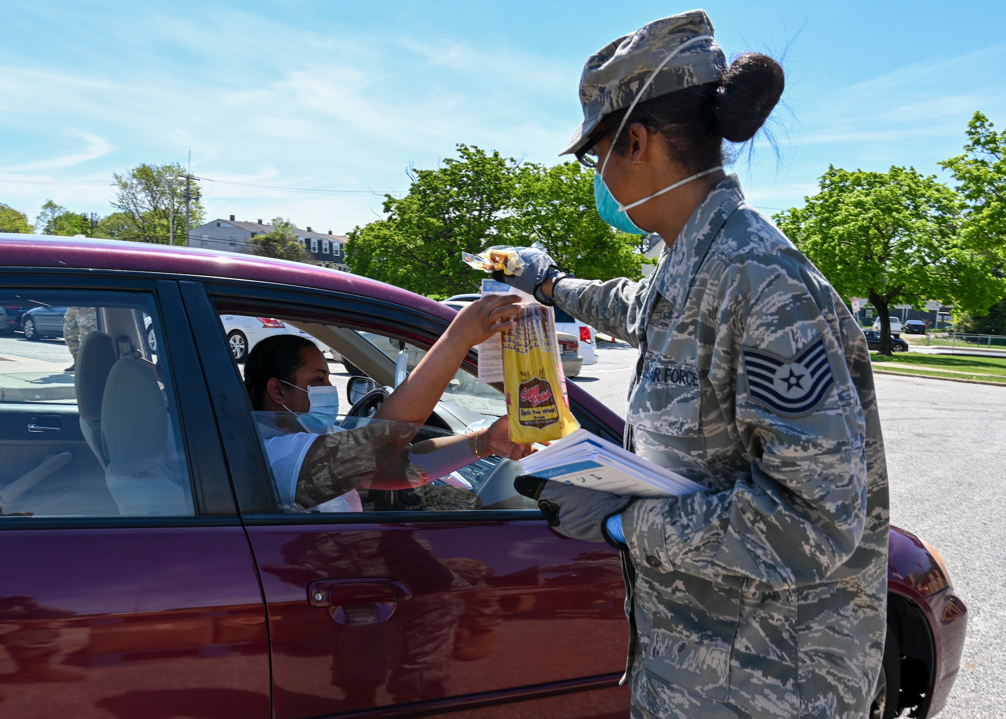 Technical Sgt. Erica Brown, command support staff assigned to the 235th Civil Engineer Flight, Maryland Air National Guard hands out bread to a member of the community while supporting efforts to distribute meals and groceries to local communities, May 2, 2020, Baltimore, Md. The program is designed to ensure citizens of the local community have food and groceries while schools and work places are closed. (U.S. Air National Guard photo by Tech. Sgt. Enjoli Saunders)
