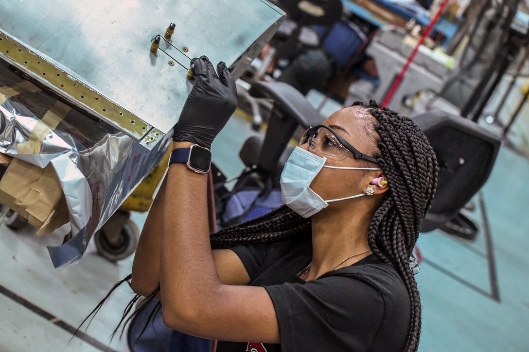 An apprentice installs forward latches on a P-3 Orion door.