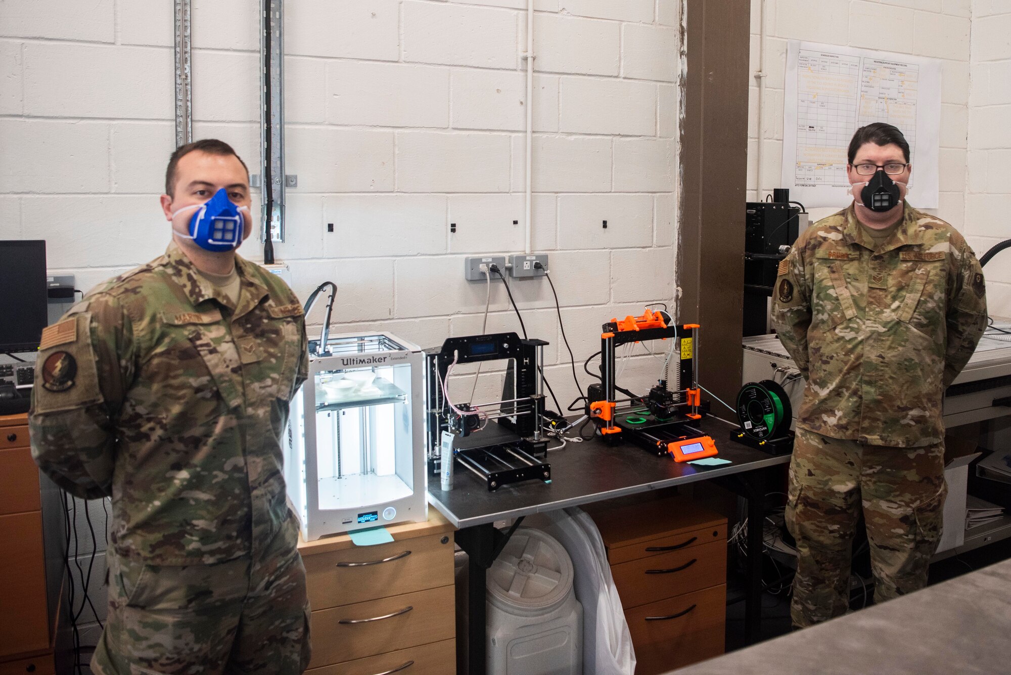From left to right, U.S. Air Force’s Senior Airman Carl Martin, 352d Special Operations Aircraft Maintenance Squadron support technician, and Staff Sgt. Alex Bruce, 352d SOAMXS MC-130J equipment custodian, stand in front of the 3D printers they use to construct plastic masks, April 27, 2020, at RAF Mildenhall, England. Bruce and Martin have produced more than 100 masks for squadron members in the past month, following DoD health guidelines on the use of cloth face coverings by using 3D printers to engineer face masks in an effort to combat the spread of Coronavirus. The 352d Special Operations Wing is the sole Air Force special operations unit in the European Theater. (U.S. Air Force photo by Airman 1st Class Joseph Barron)