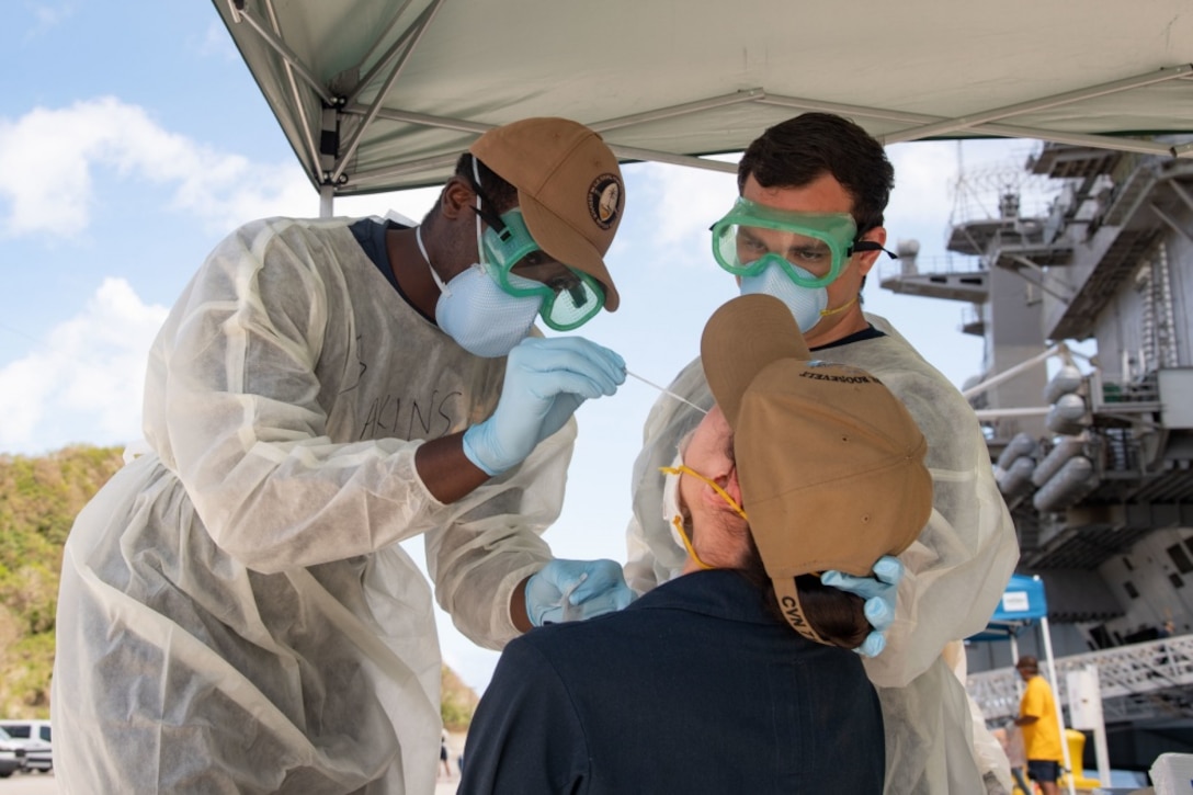 Two male Naval hospital workers swab a female sailor.