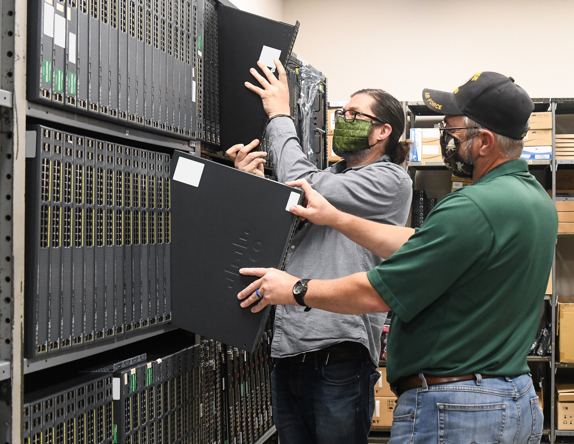 Network Operations team members Troy Smiddy, right, and Ryan Eaves, work together in a storeroom, May 5, 2020, at Arnold Air Force Base, Tenn. The AEDC Base Communications continues to provide support to AEDC during the coronavirus pandemic to ensure fellow AEDC team members have the communications resources necessary to fulfill the AEDC mission. They are utilizing social distancing and when that is not possible, masks, as risk mitigation measures. (U.S. Air Force photo by Jill Pickett)  (This image has been altered by obscuring items for security purposes and cropped to emphasize the subject.)