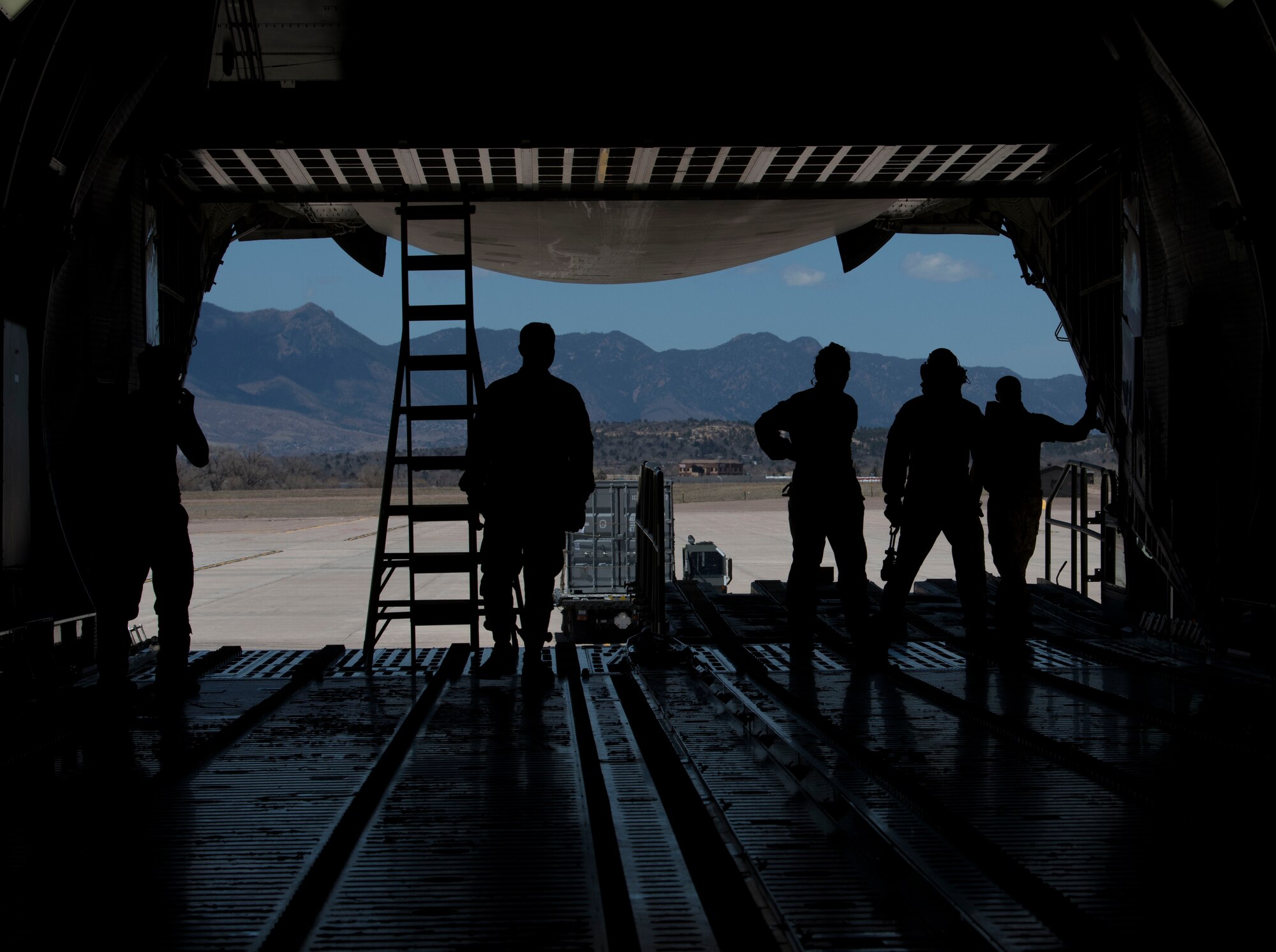 Airmen from the 21st Logistics Readiness Squadron, the 22nd Airlift Squadron watch as a K Loader is directed after putting cargo pallets onto a C-5M Super Galaxy, April 27, 2020 on Peterson Air Force Base, Colorado. The 21st LRS loaded the cargo to assist in a Space and Missile Systems Center mission to bring supplies to warfighters down range. The 21st LRS was able to coordinate with the SMC, receive the cargo, inspect it and have it on a plane in less than two weeks. This fast turnaround was to match the speed of the SMC Rapid Reaction Branch needed the cargo to be sent downrange. (U.S. Air Force photo by Airman 1st Class Andrew J. Bertain)