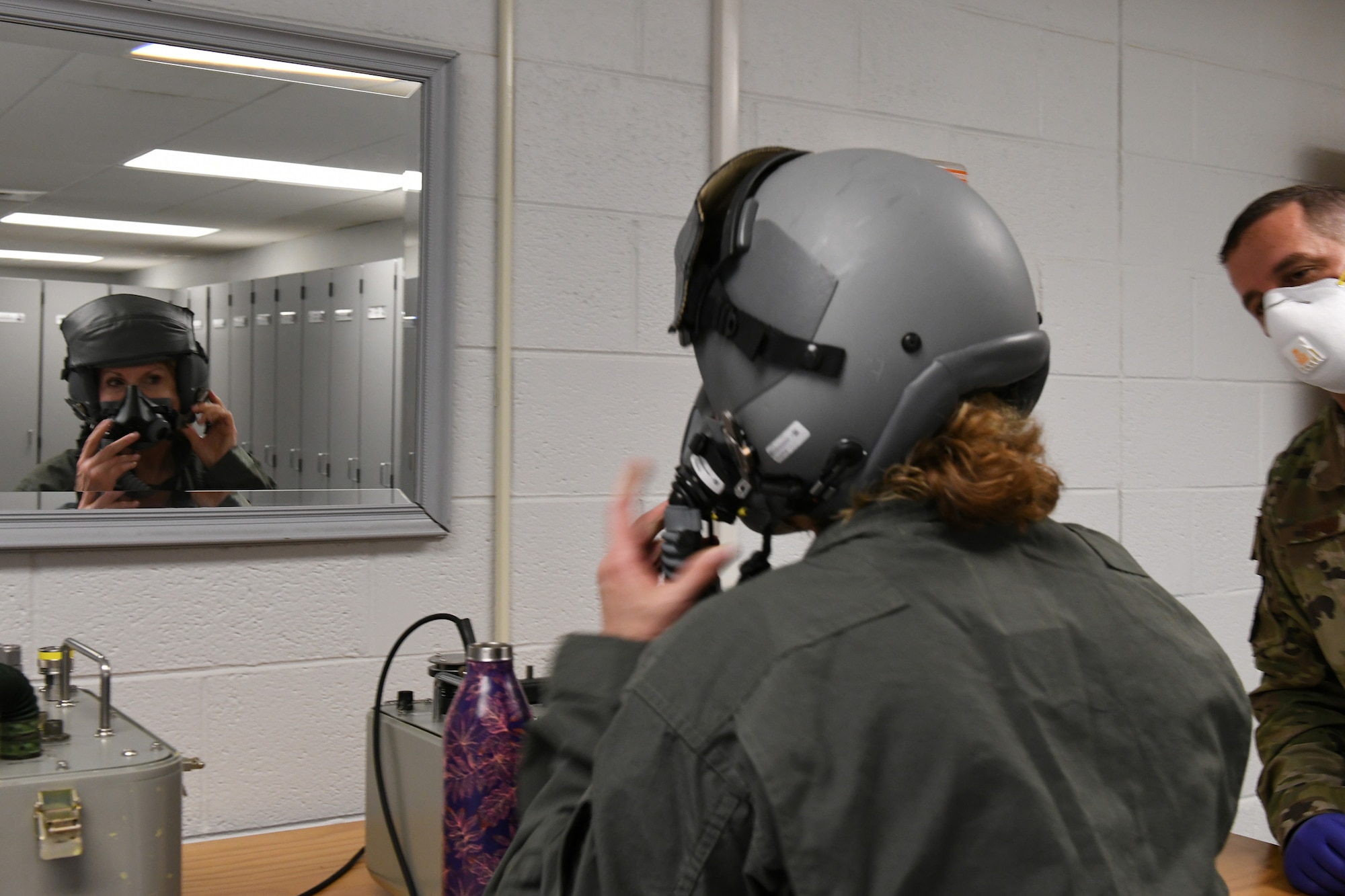 Photo shows Col. Farrell with her helmet on looking in the mirror as she fits her mask to her face.