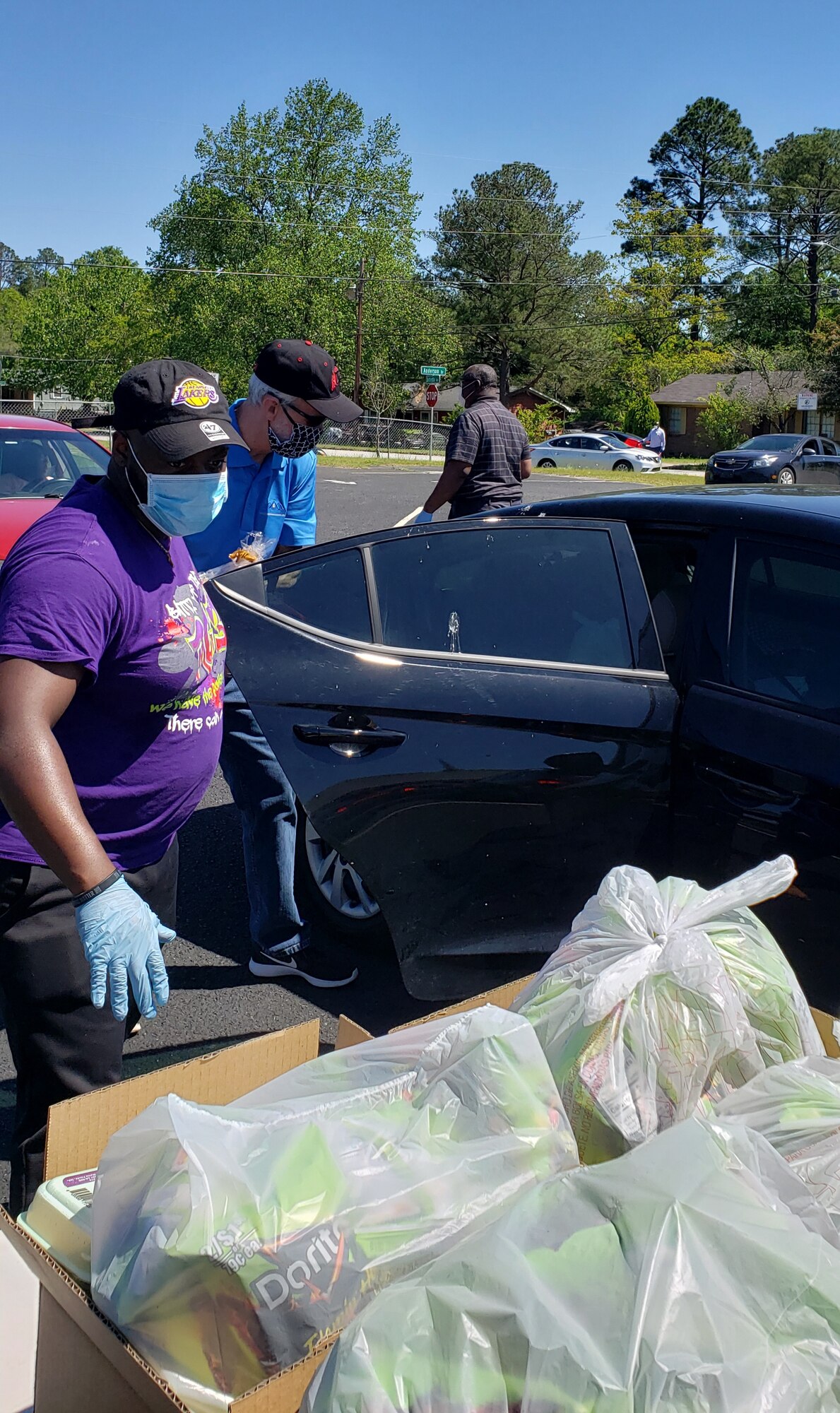 Photo shows a line of cars receiving food put out on tables.