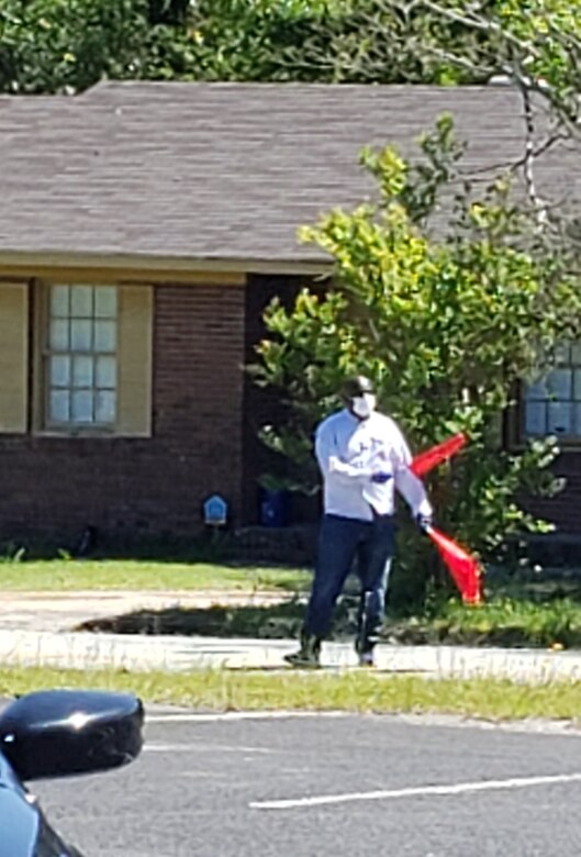 Photo shows a man holding two orange flags directing traffice.